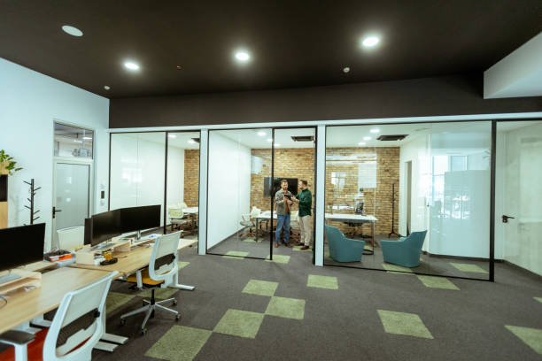Two professionals engage in a conversation while standing comfortably in an office lounge, surrounded by greenery and contemporary design elements