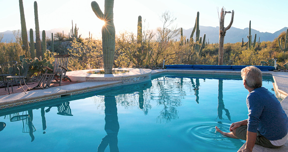 Mature man relaxes at desert swimming pool in morning light