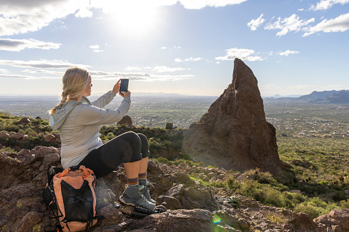 Mature woman hiker pauses in desert and takes photo of pinnacle in distance