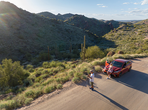 Aerial view of couple photographing in desert landscape at sunset from vehicle