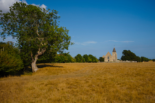 A wide view of St Clement Church in the distance with a golden field and tree in the foreground, and a deep blue sky.