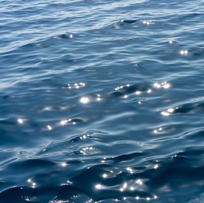 Close-up on a smooth sea surface in summer, with bright sunlight creating bright sparkling reflections.