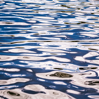 A smooth surface of water, reflecting the blue sky and clouds above.