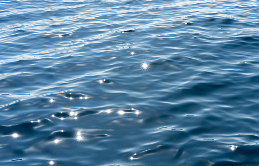 Close-up on the surface of the sea, with bright sunlight creating bright sparkling reflections.
