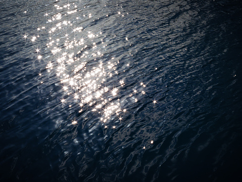 A deep blue surface of lake water, with bright sparkles of reflected sunlight creating star shapes.