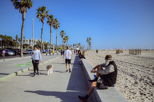 10 March 2024, Los Angeles, USA. Venice beach on a bright sunny day. Crowds of people tourists walking path along pedestrian zone of broadwalk. Cyclists ride on bicycle roadway. Beautiful oceanfront