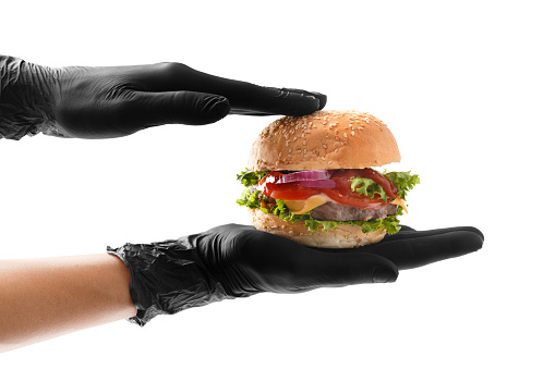 Hands in black gloves hold a juicy, appetizing beef burger on a white background. Hamburger in hands isolated. Banner, fast food advertising.