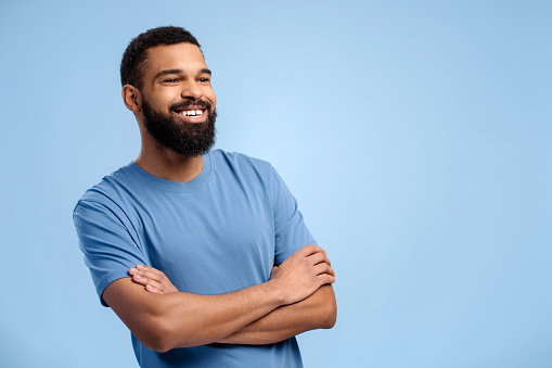 Handsome, authentic African American man wearing casual clothes with crossed arms looking away, copy space, standing isolated on blue background. Concept of advertisement, shopping