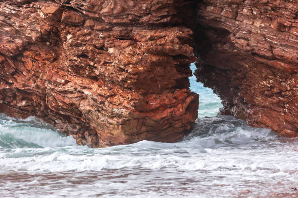 Wild beach Crvena Glavica in Montenegro. Red rocks coast arch and water waves