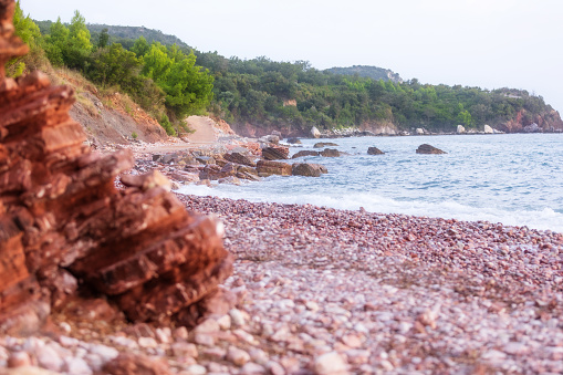Wild beach Crvena Glavica in Montenegro. Red rocks coast and water waves