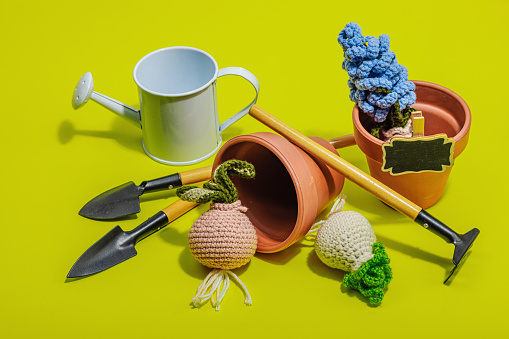 Spring planting and gardening concept. Handmade flowers with bulbs, mini tools, watering can, and buckets. Hard light, dark shadow, bright yellow background, close up