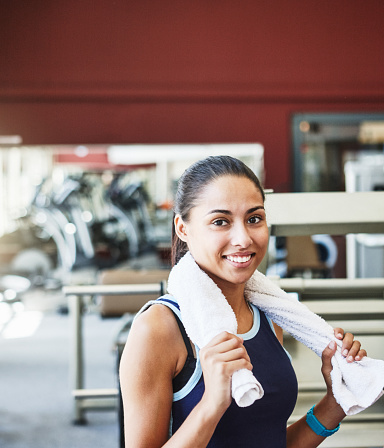 Young woman with ponytail looks radiant as she pauses with a towel at the gym.
