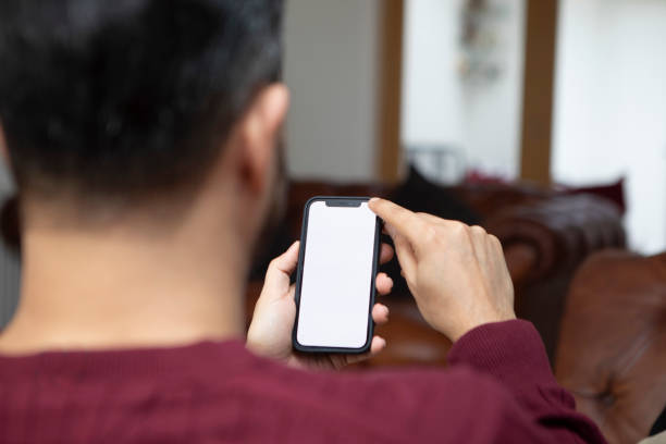 Over the shoulder view of a smart phone screen Using a smart phone to access the internet at home. The screen is blank for you own graphics. man looking at phone over shoulder stock pictures, royalty-free photos & images