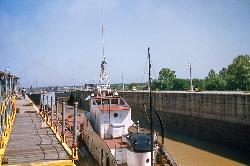 Petroleum barge and towboat locking through the Inner Harbor Navigation Canal Lock (also known as Industrial Canal Lock) in New Orleans, Louisiana, USA headed toward the Mississippi River in the background. The canal connects the Mississippi River with Lake Pontchartrain and the Gulf Intracoastal Waterway and associated port facilities. Photo take in 1953 before the Claiborne Avenue Bridge was built in 1957.