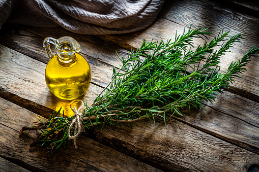 Bunch of fresh organic rosemary and olive oil bottle on rustic table