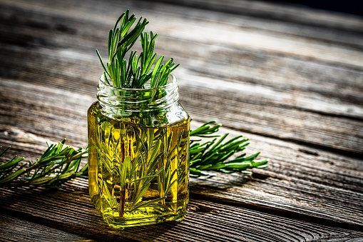 Olive oil bottle with rosemary twigs inside on rustic table