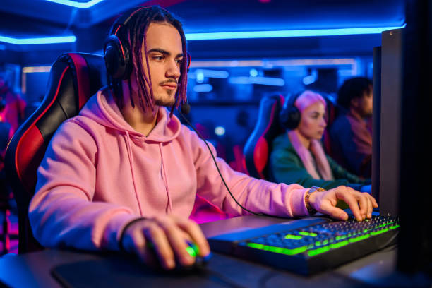 istock Young man with dreadlocks and mustaches playing video games in an internet cafe 2102343346