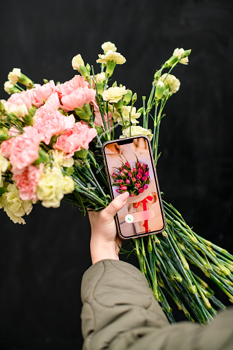Mobile phone screen with a picture of a large bouquet of red flowers and bouquet of the pink flowers in the hands of a girl