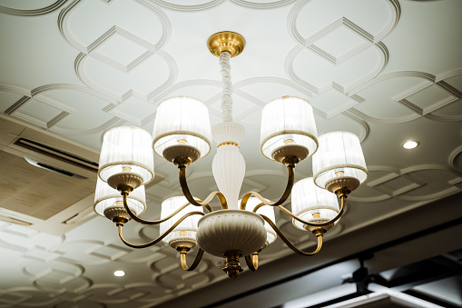 The ceiling fixture in the room is a chandelier providing lighting through electricity. Its metal structure adds symmetry to the space, creating a warm ambiance for any event