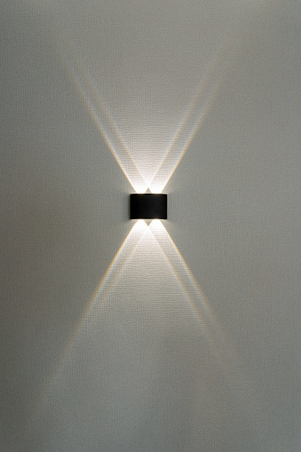 A black wall light illuminates a gray wall, creating a symmetrical circle of light. The lens flare adds a unique touch against the skys tints and shades, in contrast with the surrounding darkness