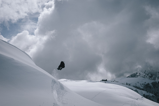 Backcountry snowboarder jumps into air through fresh powder snow