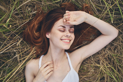 happy woman lies in the hay outdoors in a white dress and gestures with her hands. High quality photo