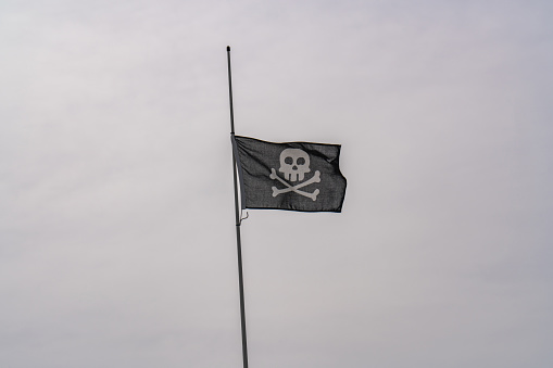 Pirate flag waving in the gray sky, skull and crossbones