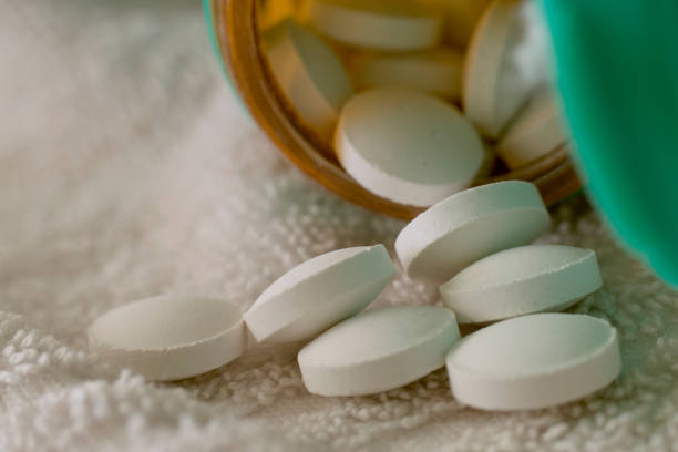 white pills coming out of a bottle\non a white surface
