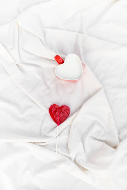 istock Lollipop and cup in hearts form on a white satin fabric 2102400562