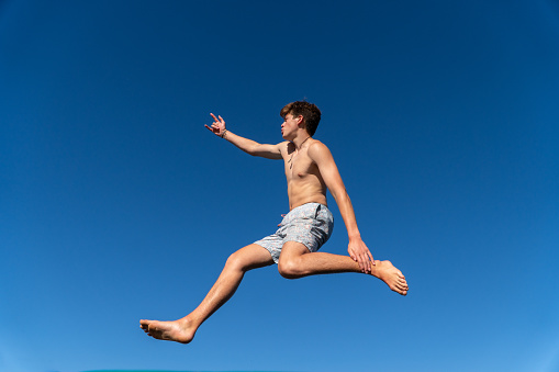 A happy young man jumps and dances against a backdrop of blue sky on a summer day.