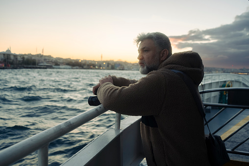 thoughtful wandering man looking at the sunset view of istanbul from a ferry. With a bag on his shoulder and a camera in his hand, he looks around. İstanbul