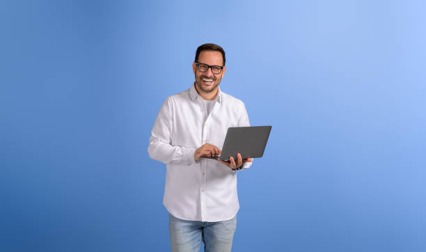istock Smiling young businessman doing online research over laptop while posing on isolated blue background 2102422895