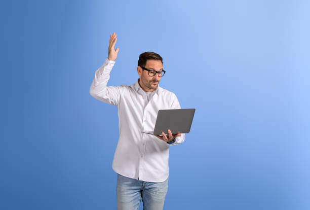 istock Young businessman raising hand while discussing over video call on laptop against blue background 2102423265