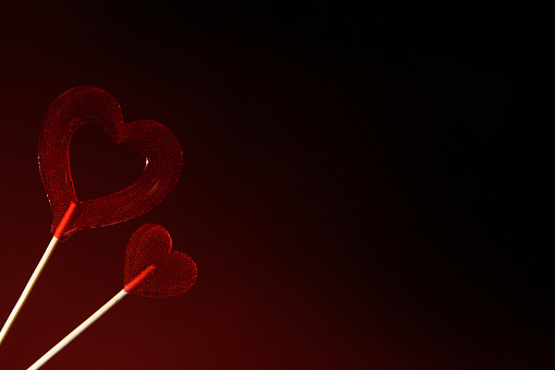 Love. Two red transparent heart-shaped lollipops on a dark red background. Horizontal banner for Valentine's Day.