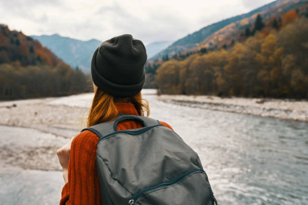 istock woman in a sweater cap with a backpack on her back mountain river in nature 2102437020