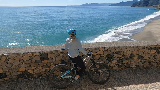 Woman mountain biker rides walkway above sea and beach