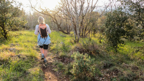 Mature woman hikes pathway in lush meadow in morning light
