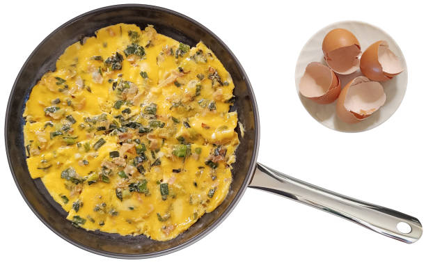 Delicious gourmet breakfast, the freshly fried scrambled eggs, prepared with chopped up and caramelized scallions and smoked pork ham, done in a new, modern, large, heavy duty, non-stick ceramic coated black frying pan, with crushed empty chicken eggs shells on white ceramic plate set beside, isolated on white background, viewed directly above.