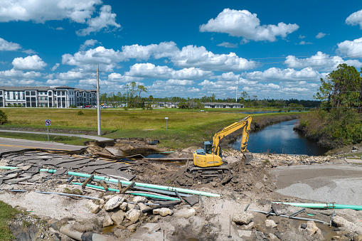 Destroyed bridge after hurricane flooding in Florida. Construction equipment at roadwork site. Reconstruction of damaged road after flood water washed away asphalt.