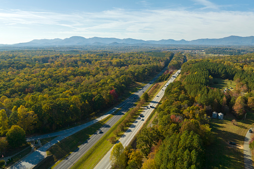 View from above of busy american highway with fast moving traffic between autumn woods. Interstate transportation concept.