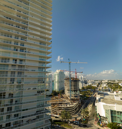 New construction site of developing residense in american urban area. Industrial tower lifting cranes in Miami, Florida. Concept of housing growth in the USA.