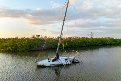 Capsized sunken sailing boat left forsaken on shallow bay waters after hurricane Ian in Manasota, Florida.