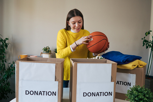 Young woman puts a basketball into a cardboard donation box