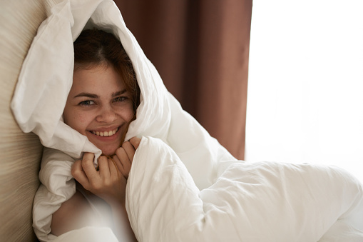 cute woman tied up under blanket in bed in the morning near window cropped view. High quality photo