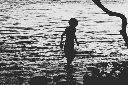 A young boy plays in a lake at dusk.