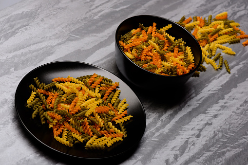 delicious colorful Italian pasta in two black ceramic plates on grey textured background, side view