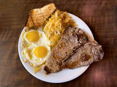 An American breakfast of a T-bone steak, eggs, hash browns and white bread