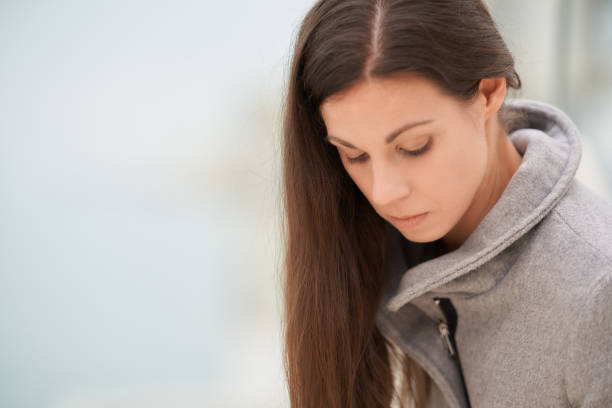 istock Young woman in a gray coat looking down thoughtfully, with a blurred background. 2102513827
