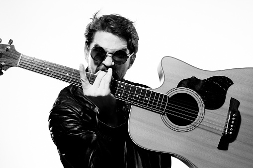 A man holds a guitar in his hands music emotions black leather jacket dark glasses studio light background. High quality photo