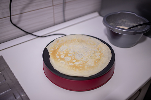 Woman making delicious crepe on electric pancake maker